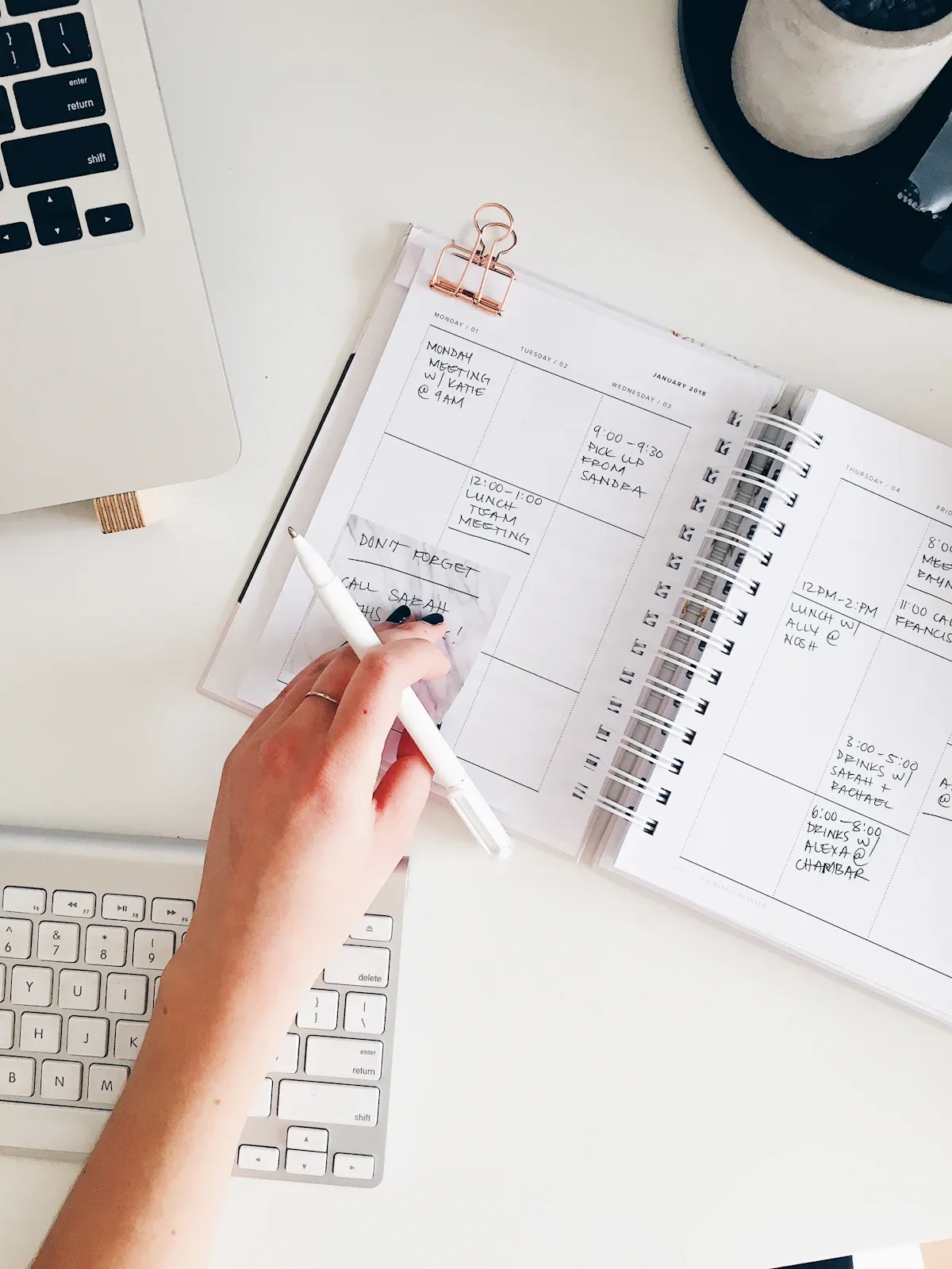 A hand writing in a planner notebook beside a keyboard