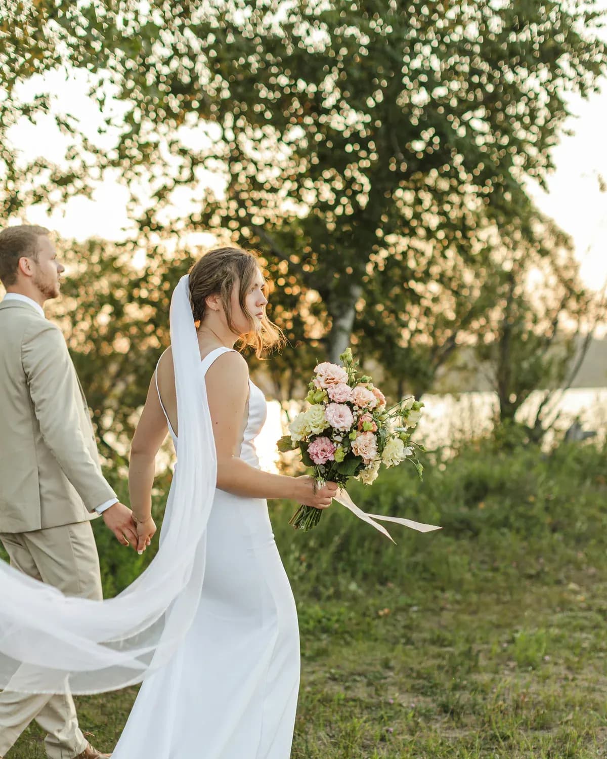 Bride walking with her bouquet beside the groom at sunset