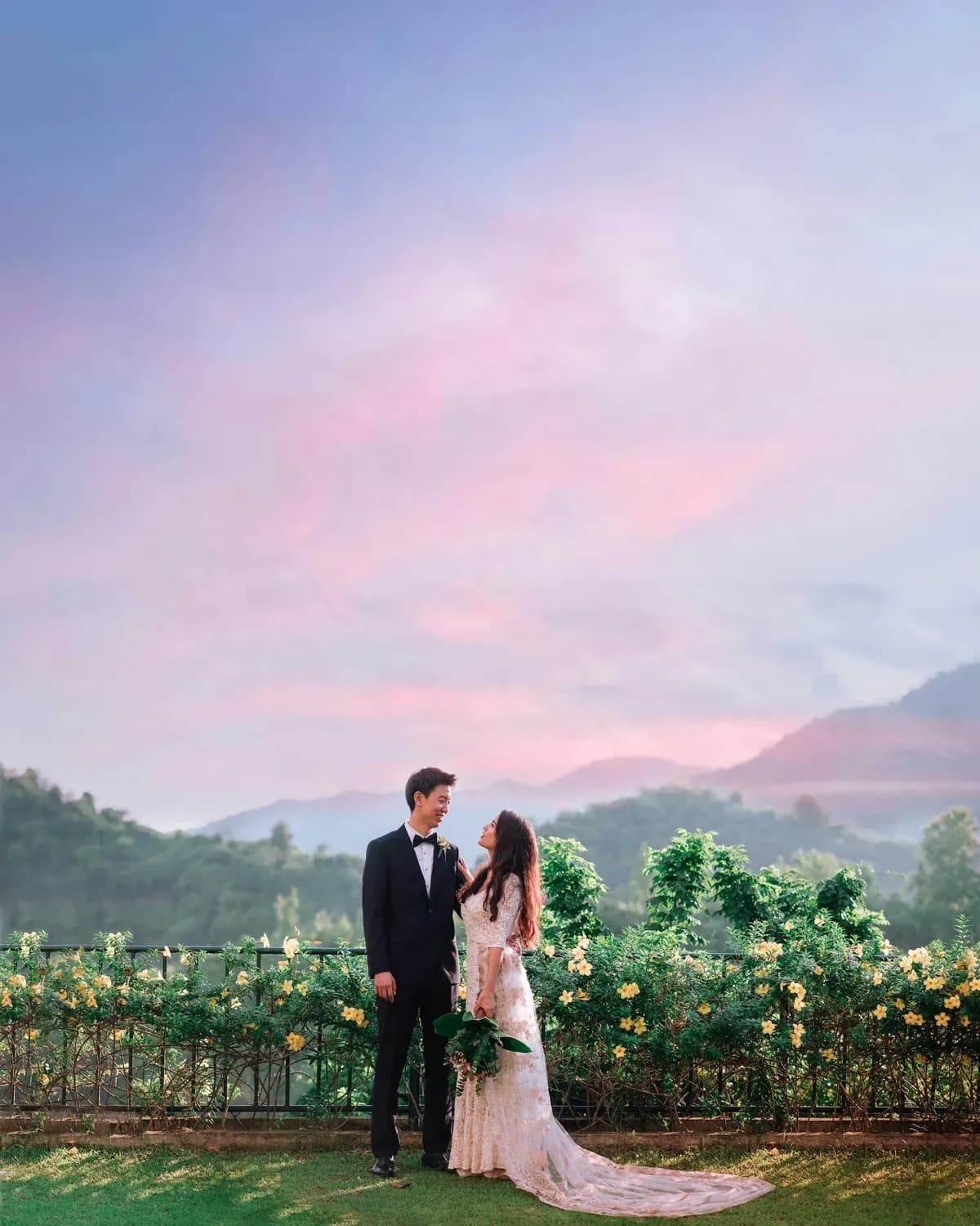Couple standing in a rose garden under a pink sunset sky